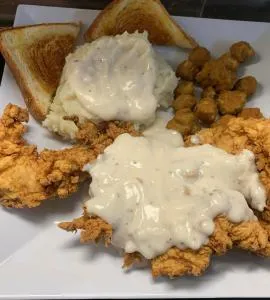 A breaded and deep-fried chicken breast served with mashed potatoes with gravy or fries.